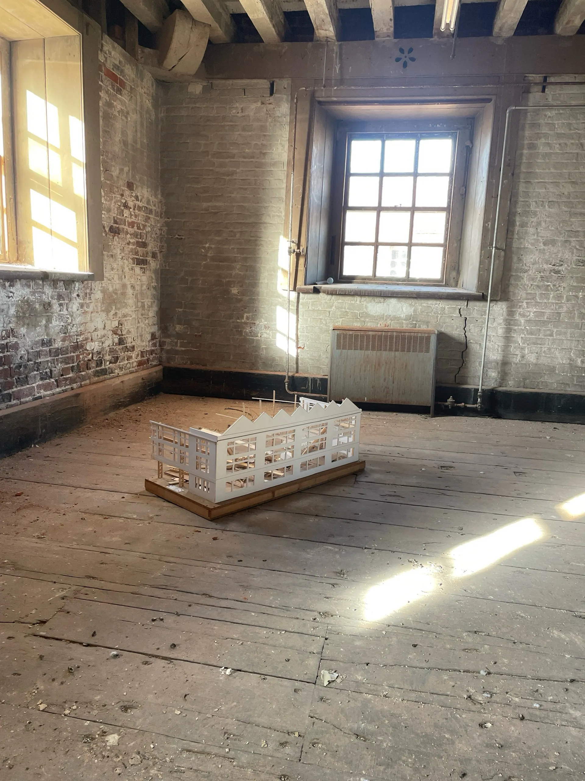 A white architectural model of Boathouse 5 on the floorboards of Storehouse 9, lit by tall windows