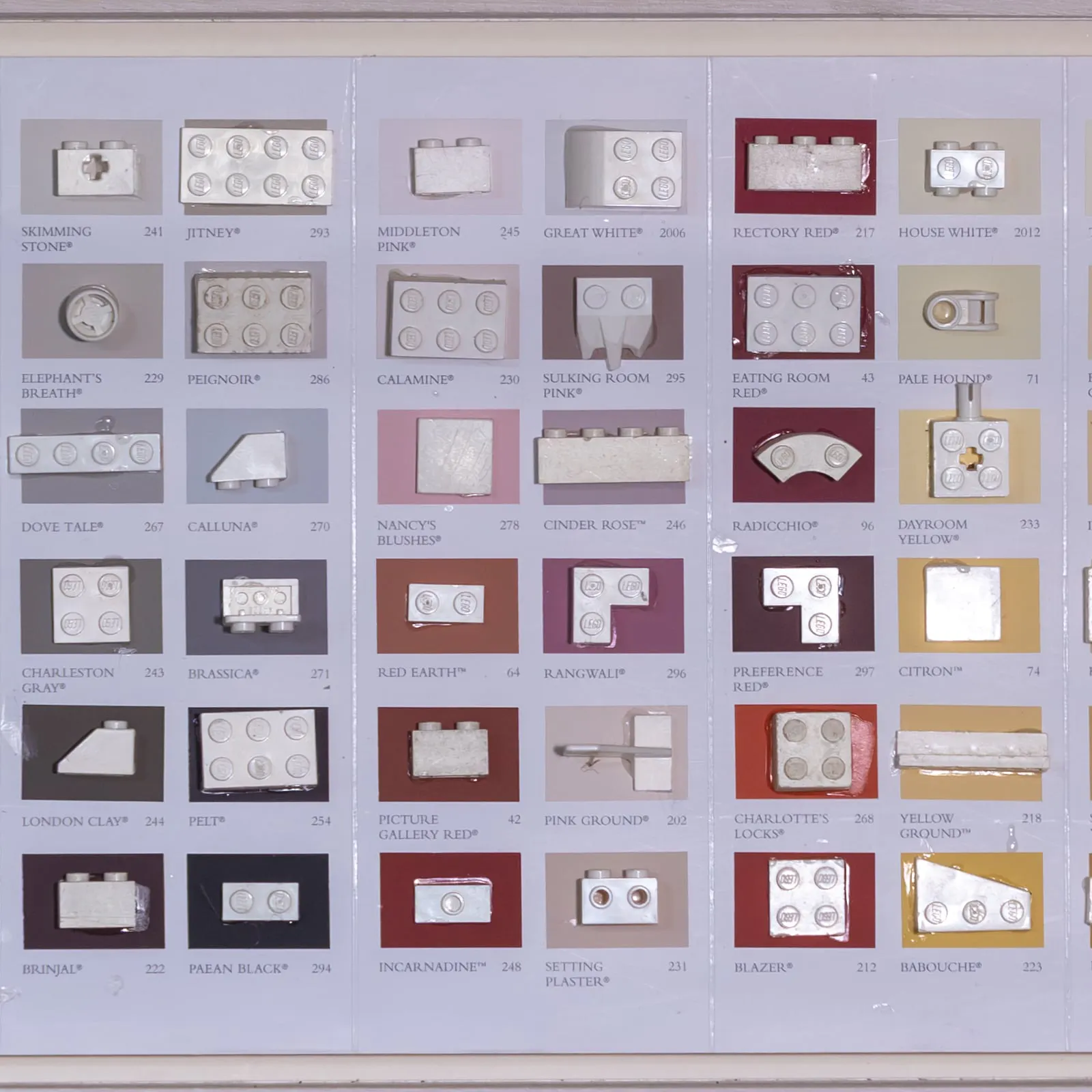 White LEGO pieces on a paint chart of named colours, each swatch labelled beneath