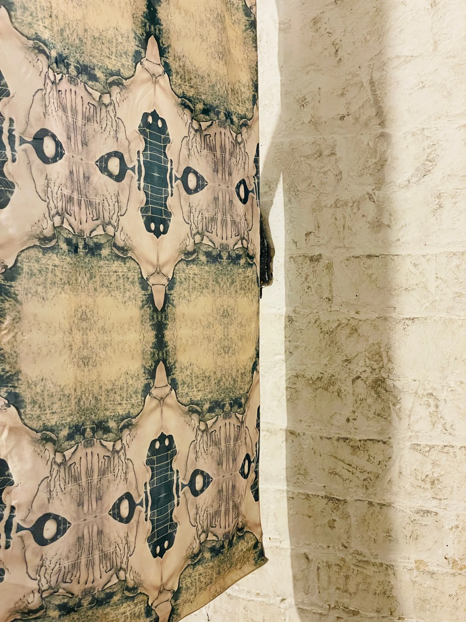 Printed silk in cream, pink and teal hung beside a textured wall