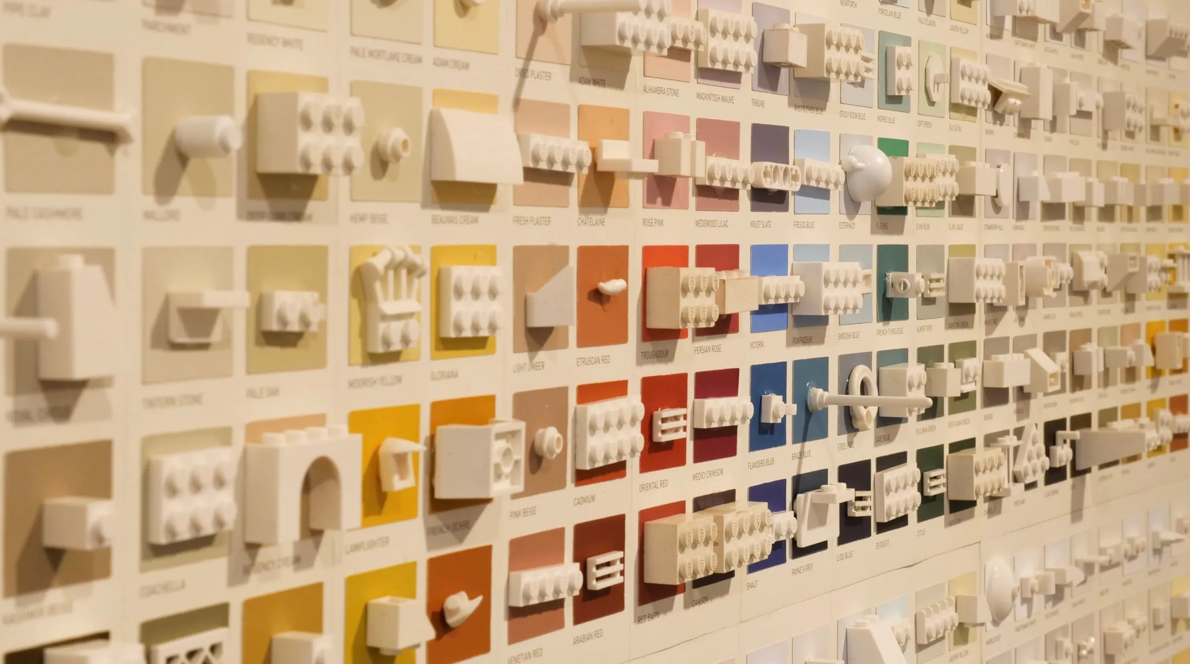 White LEGO pieces mounted across a full-colour paint chart on a wall, seen at an angle