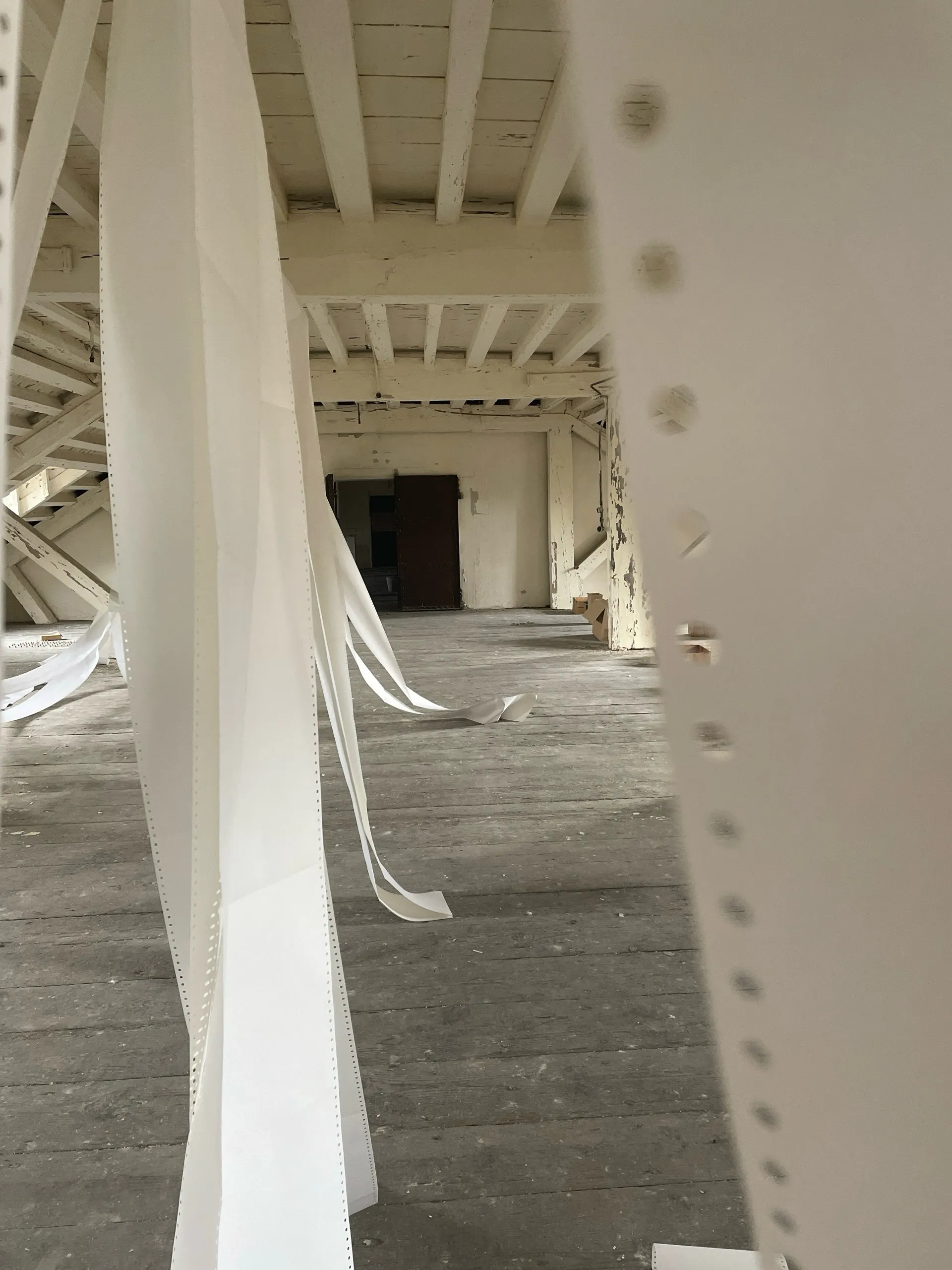 Long strips of perforated continuous-feed paper hanging from the joists and trailing across bare floorboards