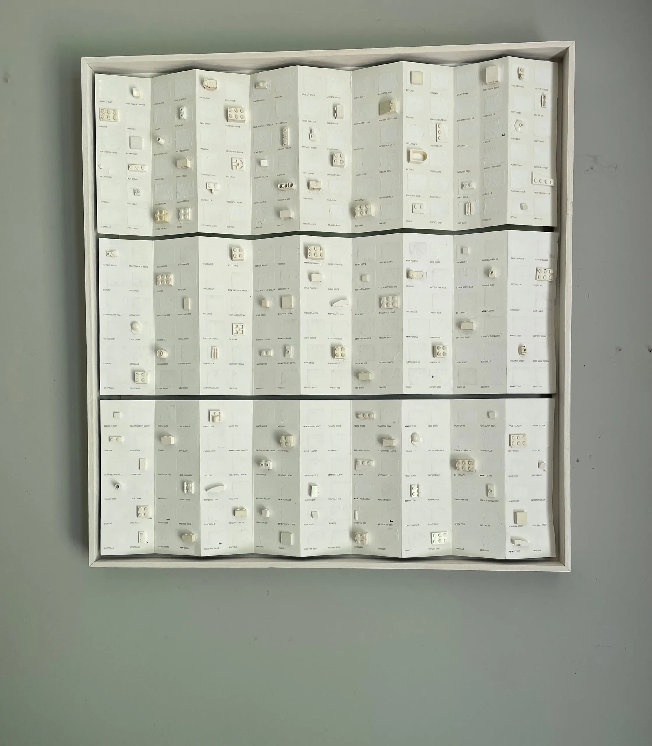 A framed panel of white paint chart, its colour removed, with pale LEGO pieces across the grid