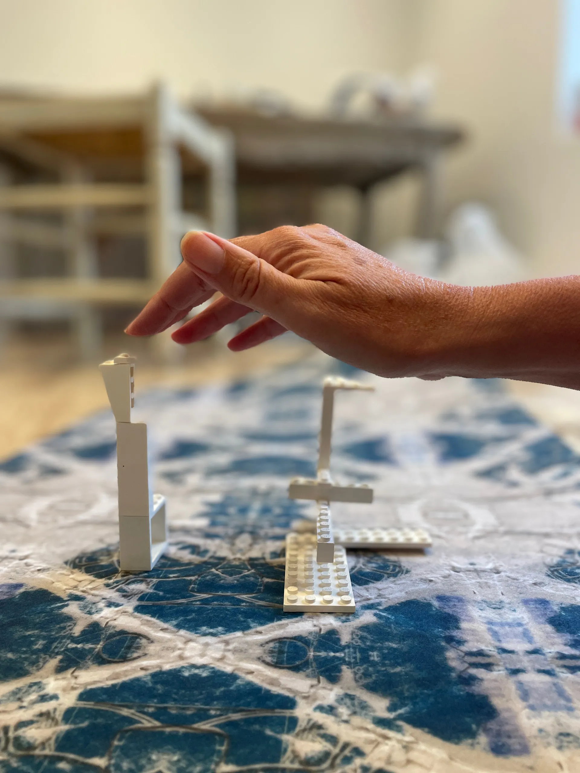 A hand reaching over small white architectural models standing on printed cloth