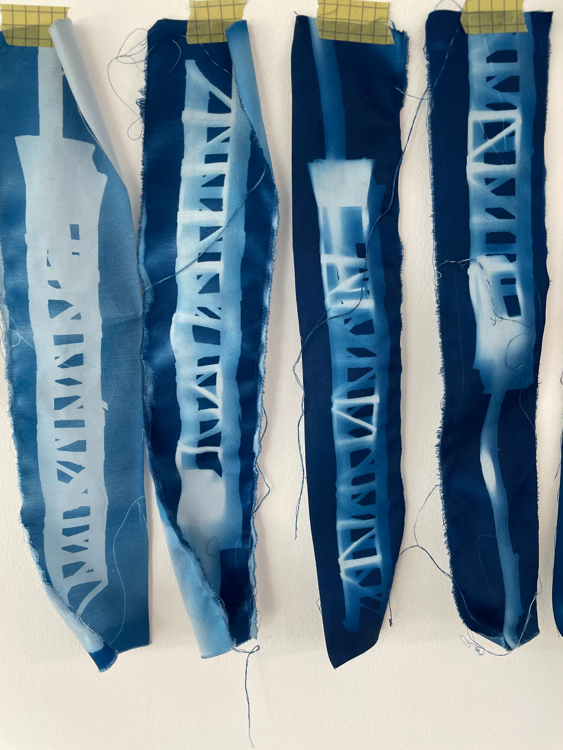 Exposed cyanotype strips taped to a white wall to dry