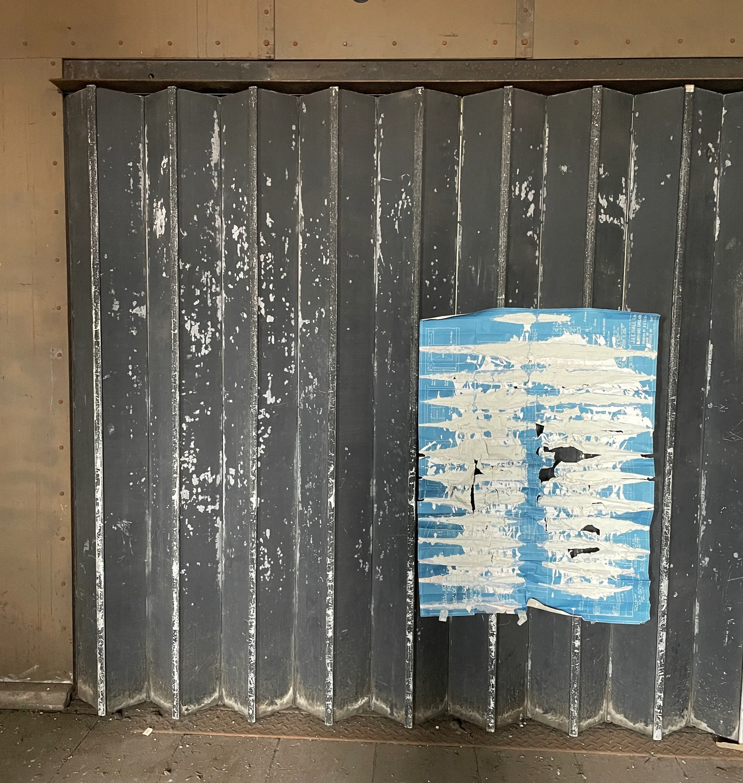 A blueprint-and-plaster work mounted on a metal shutter