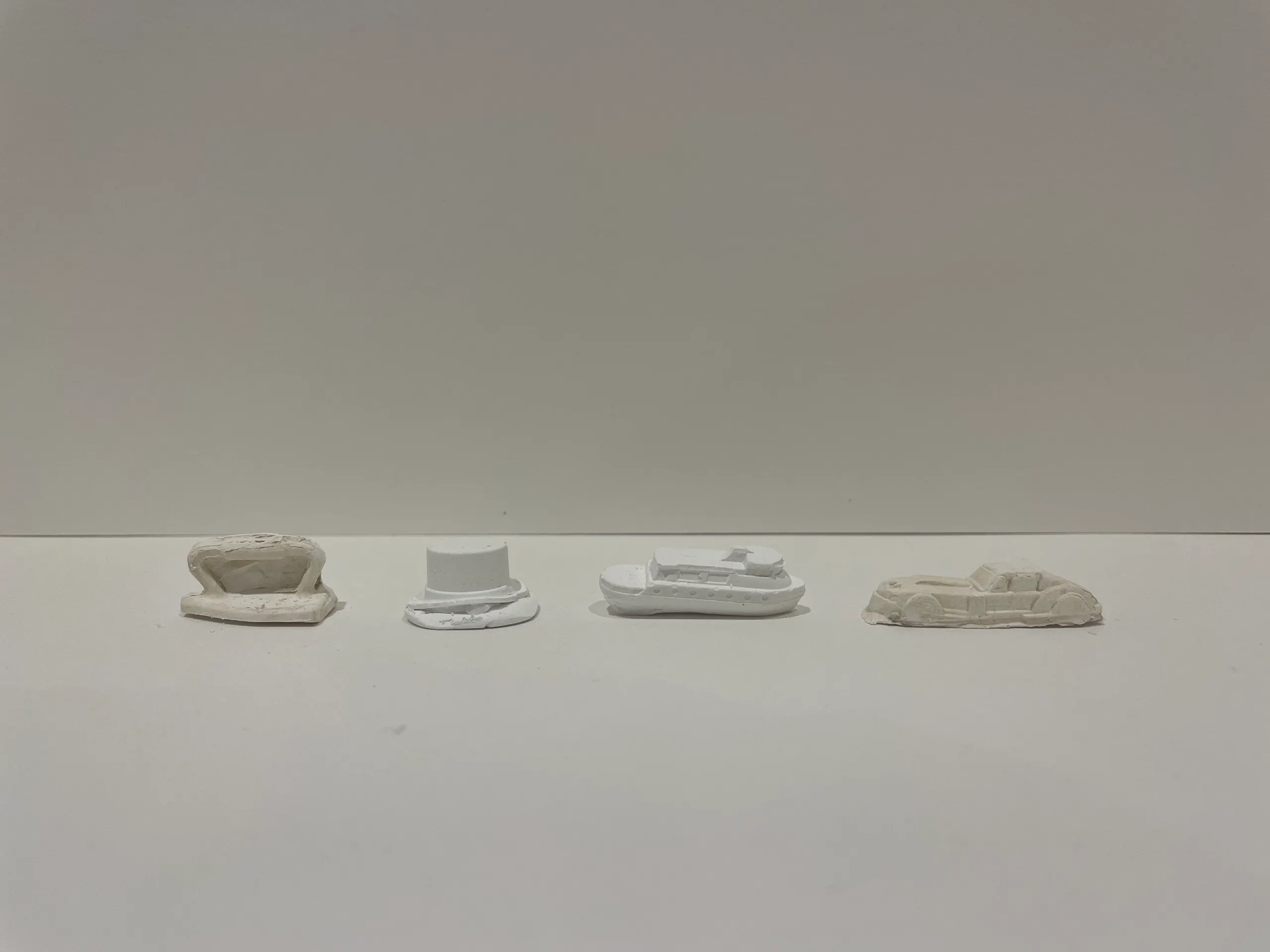 Four cast Monopoly tokens on a white shelf