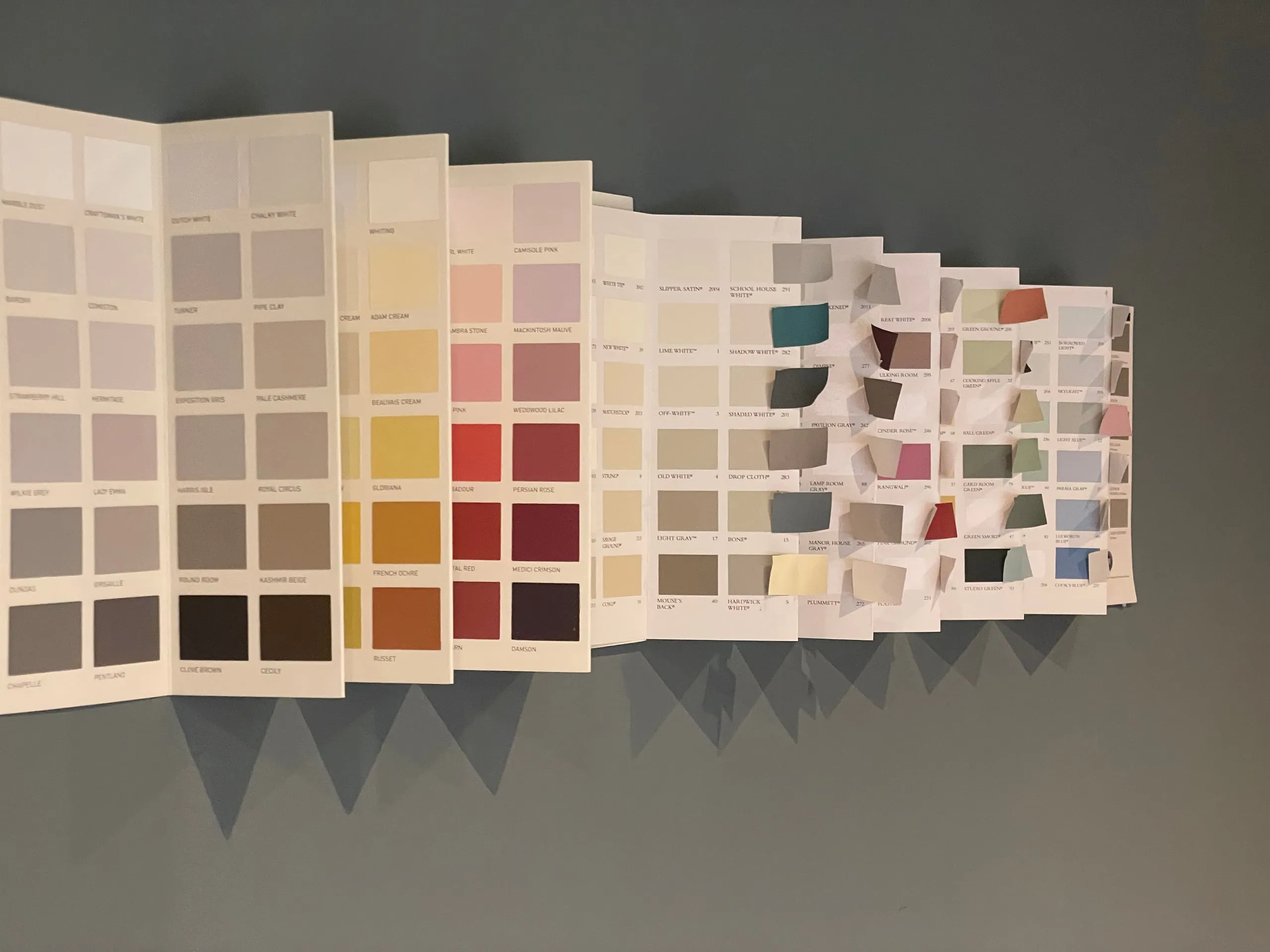 Paint charts fanned open across a grey wall, showing hundreds of colour swatches