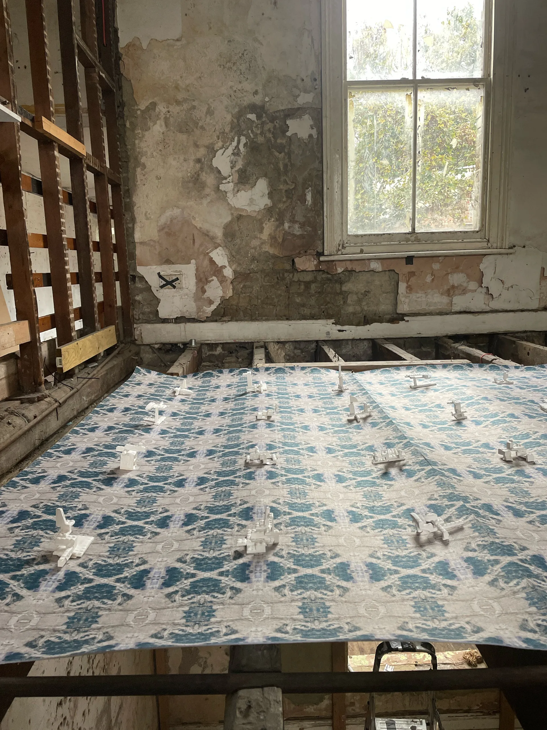 Patterned cloth laid across open floor joists in a derelict room, window light behind