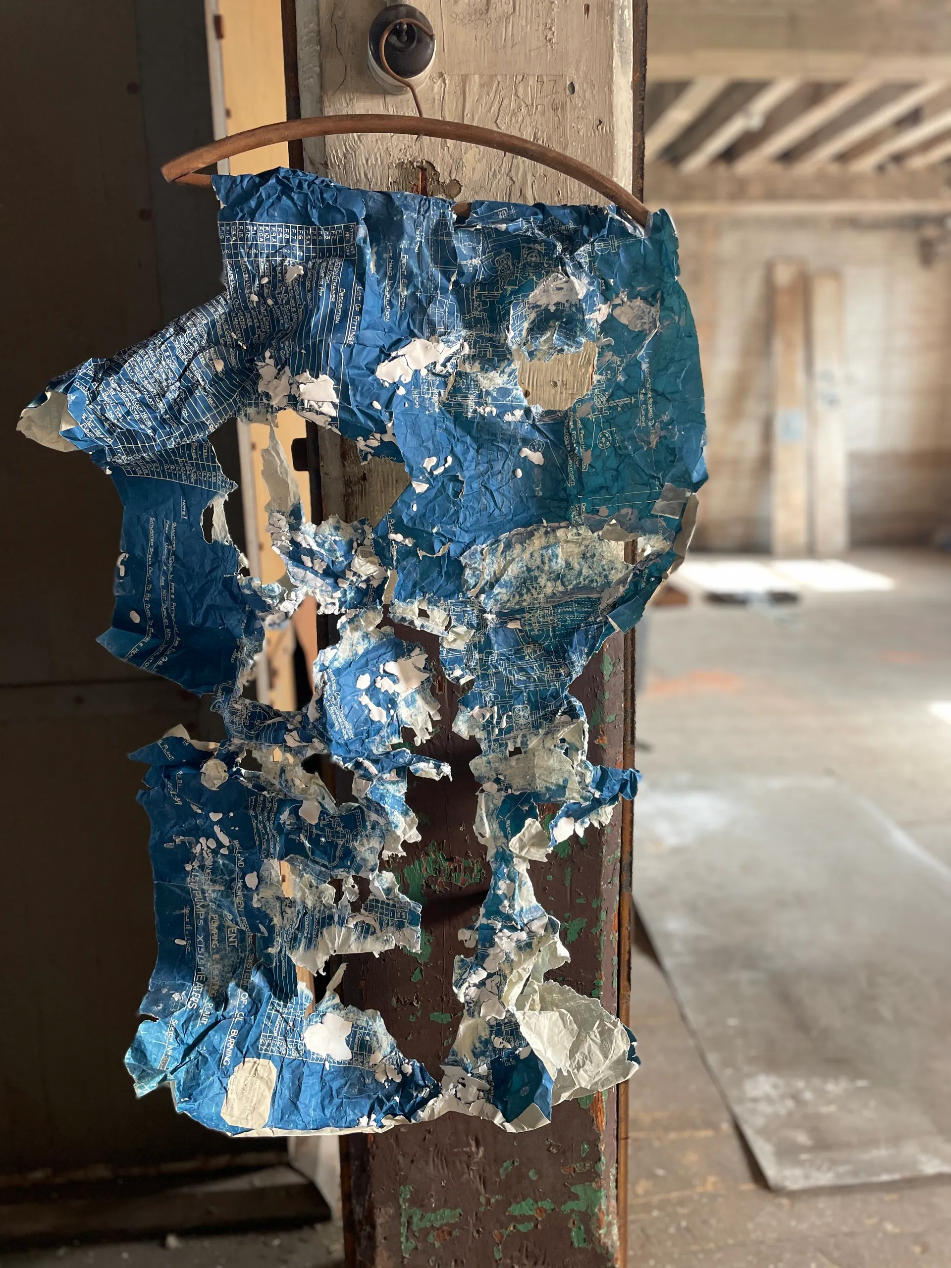 A torn blueprint-and-plaster work hanging in the space