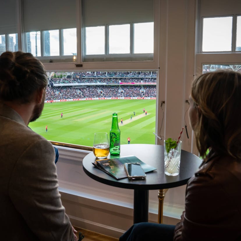 man and woman watching cricket from private box