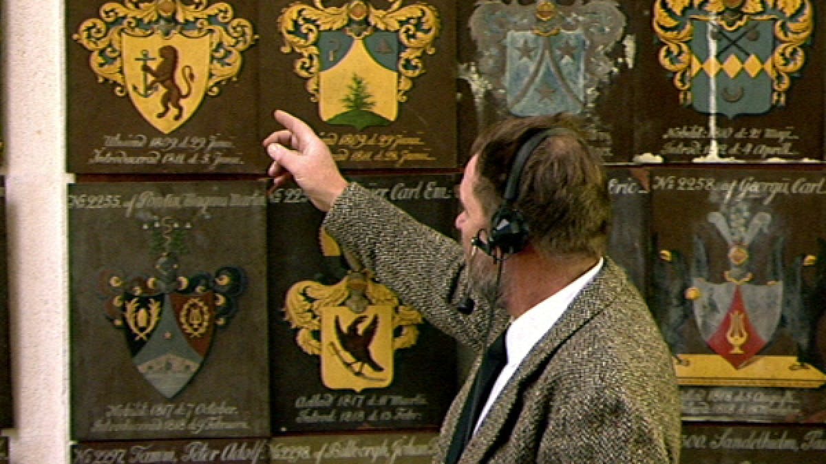 TV presenter pointing at old-fashioned crest 