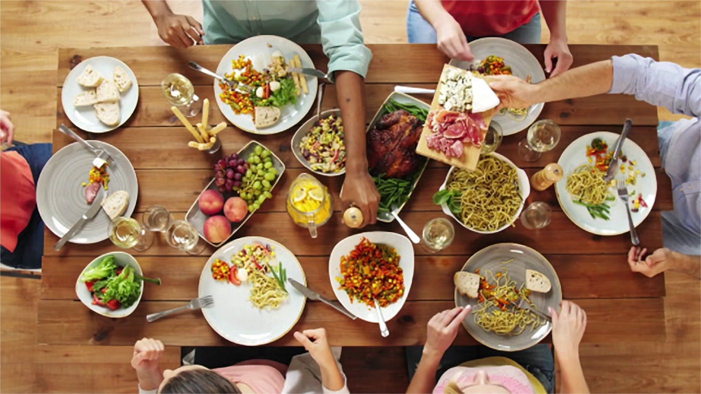 Image of dinner table with  people reaching for array of different dishes. 