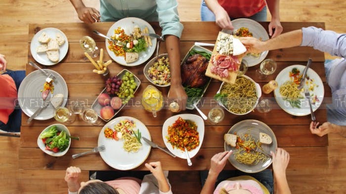 Image of dinner table with  people reaching for array of different dishes. 