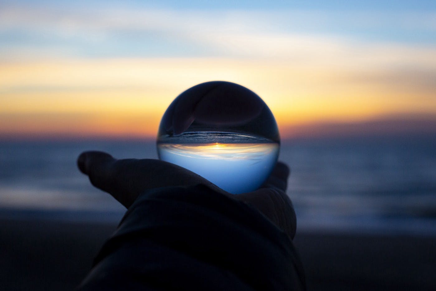 Image of a man holding out a glass ball in front of a sunset. 
