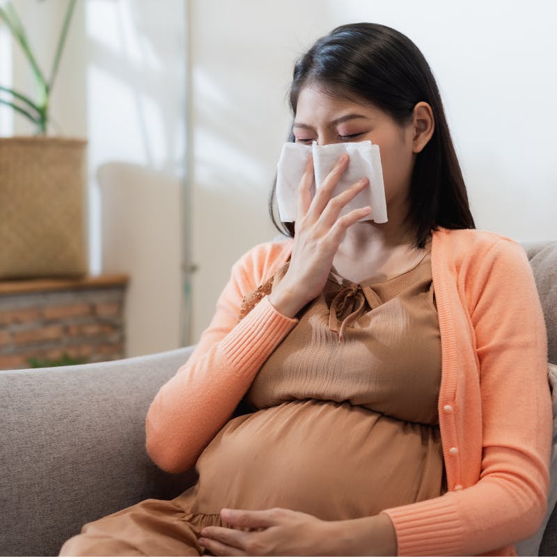 pregnant woman holding tissue to her nose