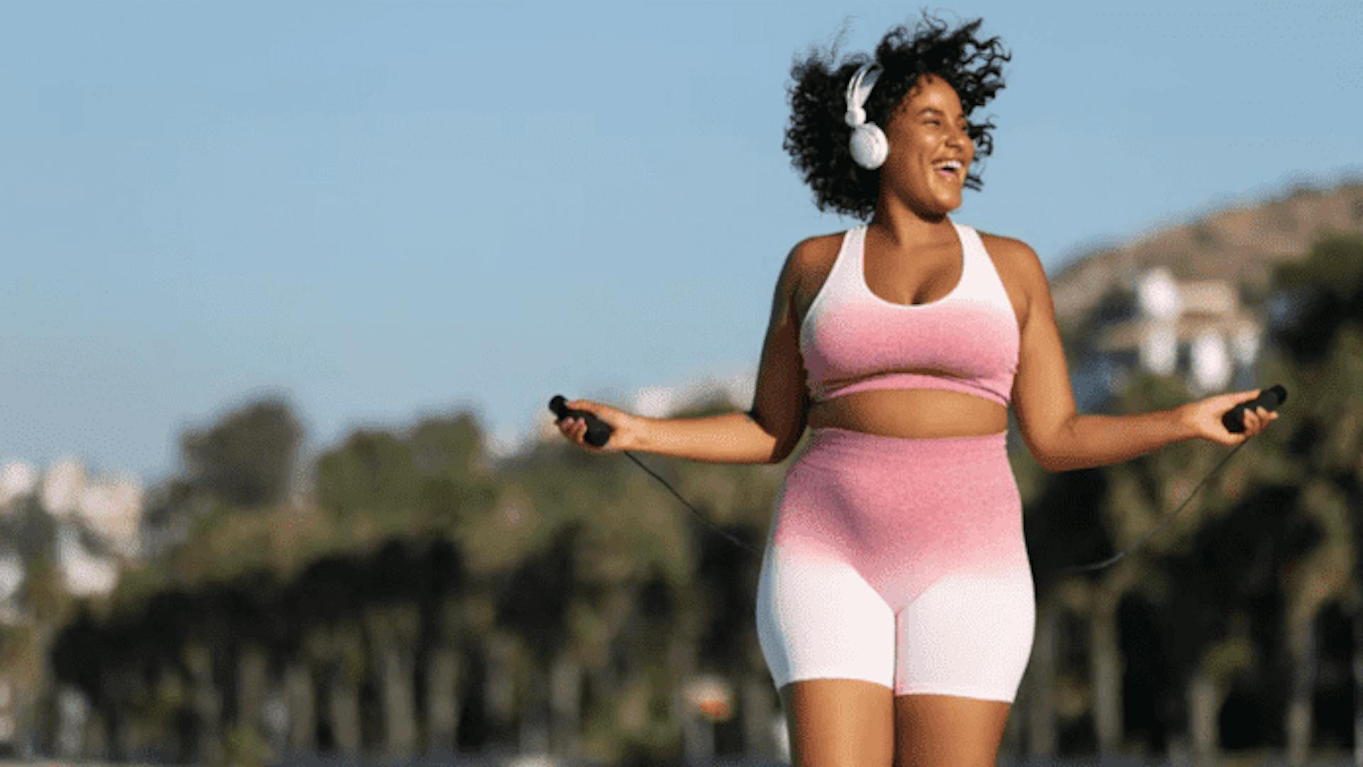 mulher preta sorridente se exercitando ao ar livre, pulando corda