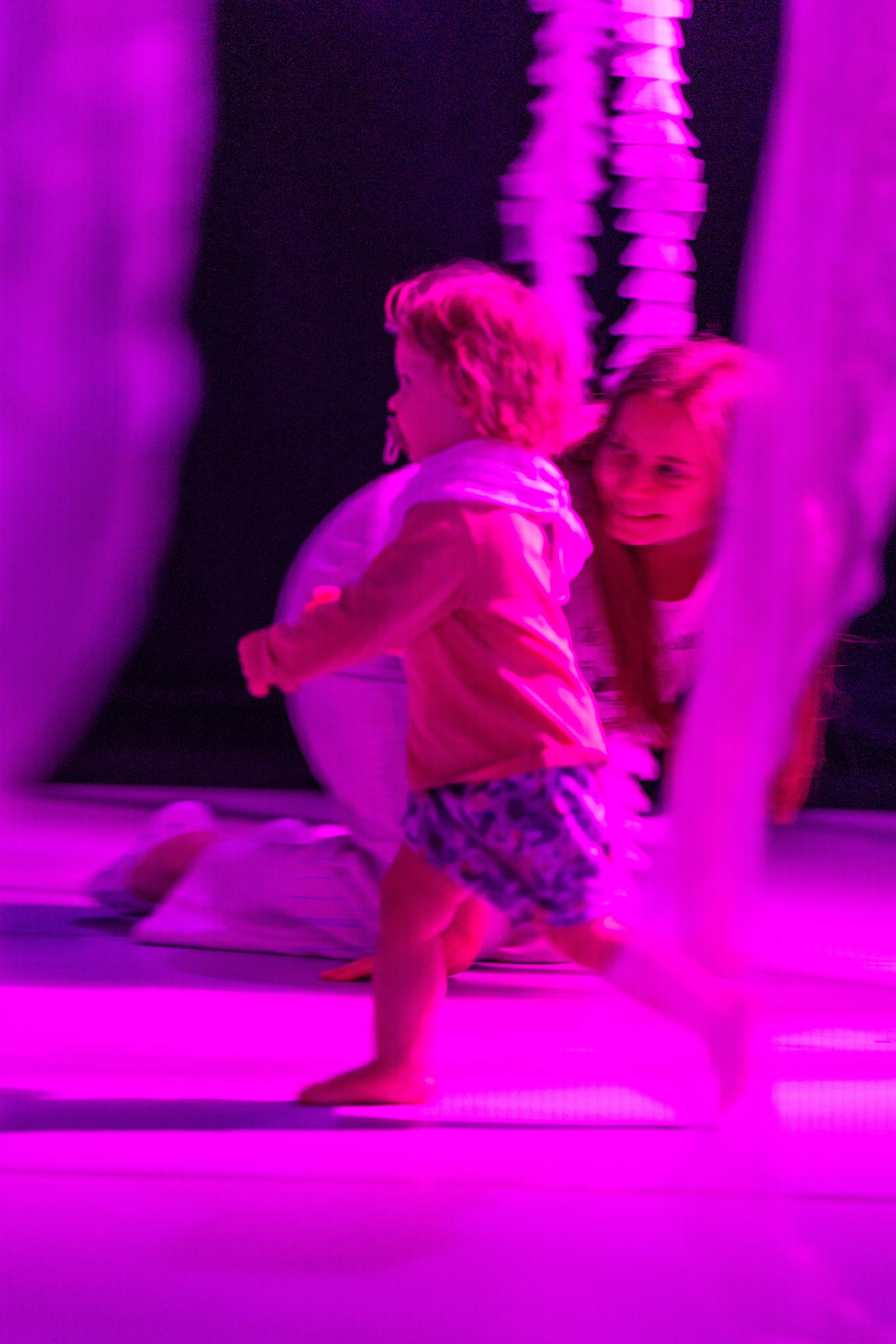 A young child running in a performance space that is lit up in pink