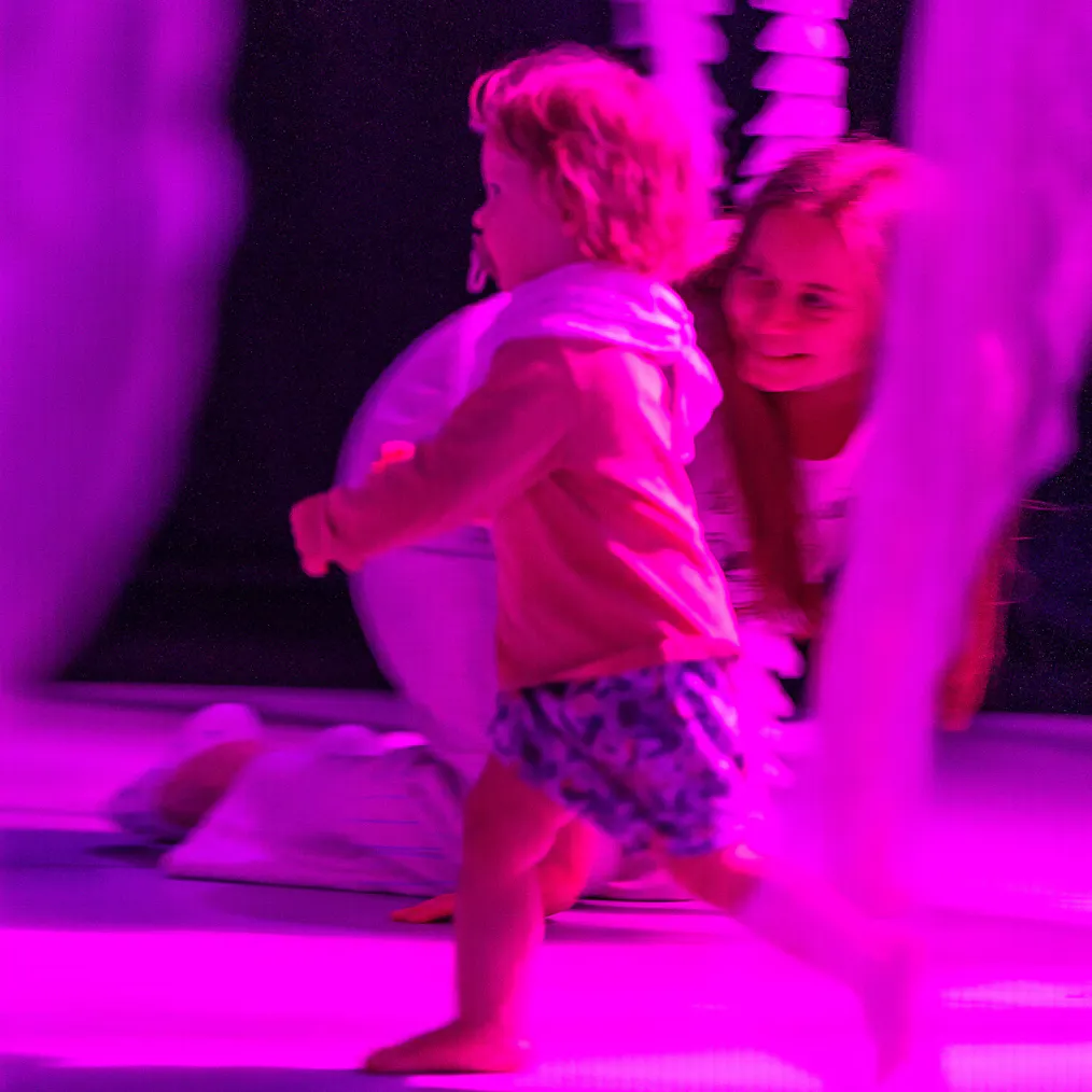 A young child running in a performance space that is lit up in pink