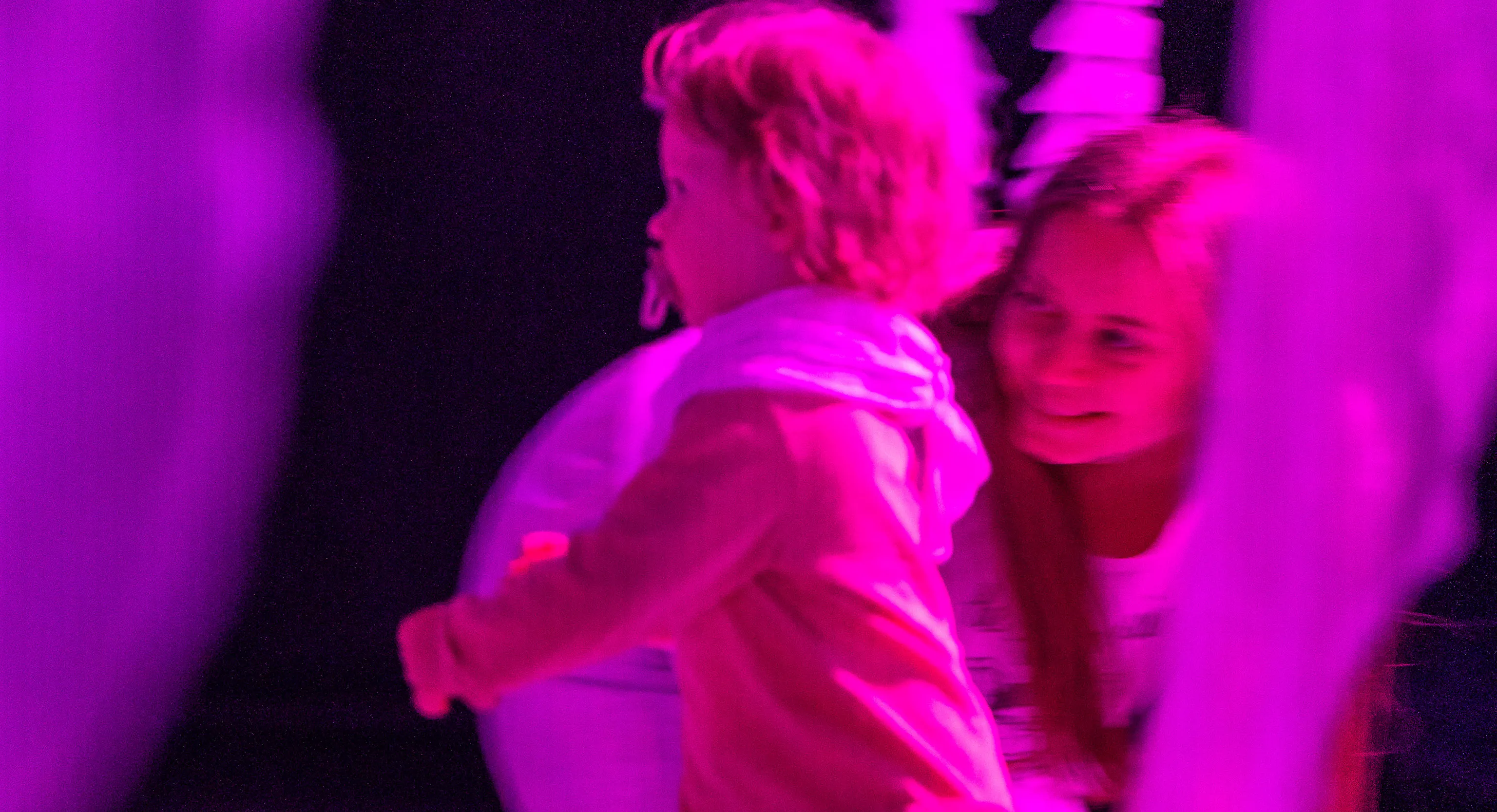 A young child running in a performance space that is lit up in pink