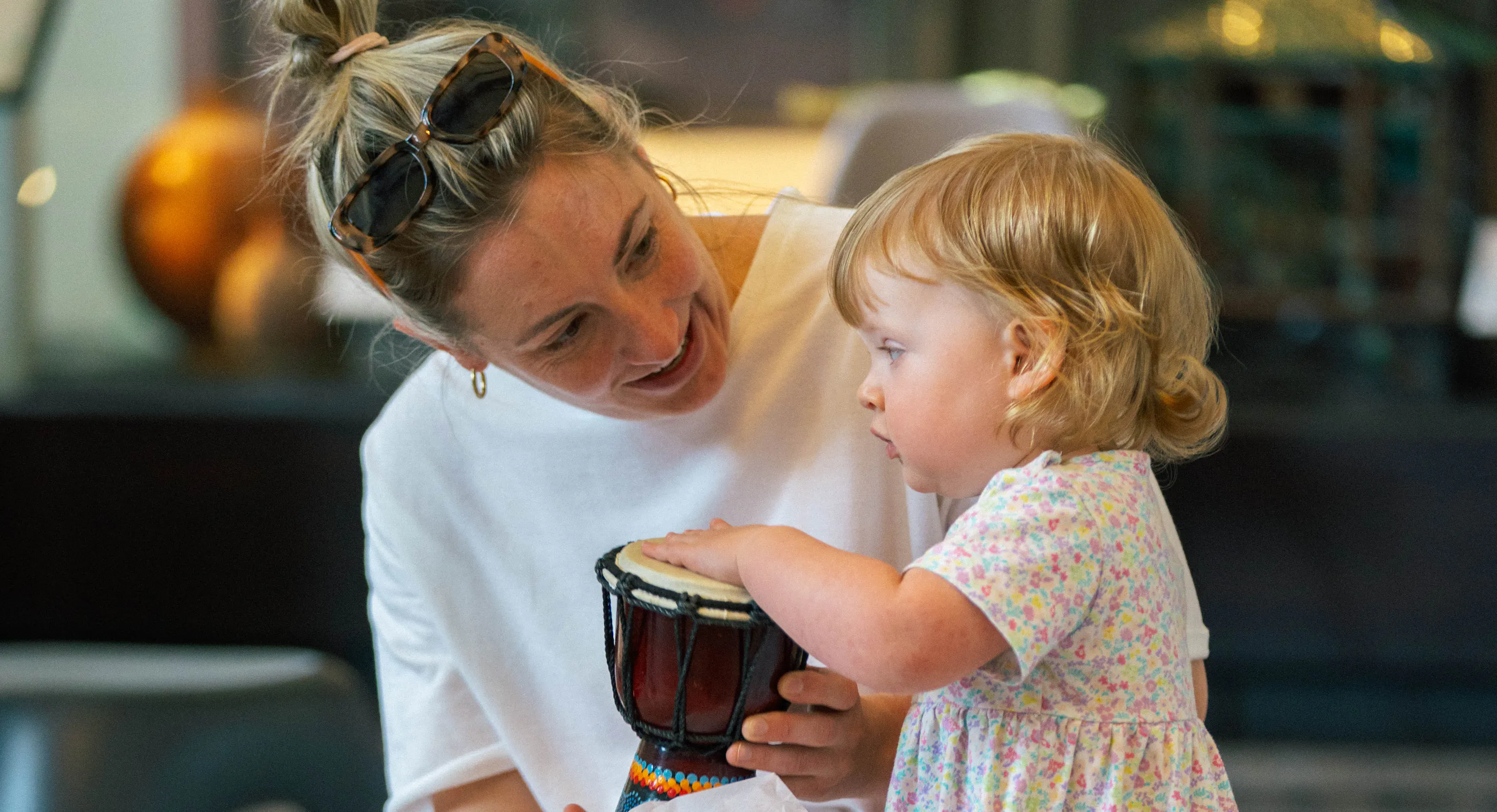 A young child and their parent/carer holding a drum together