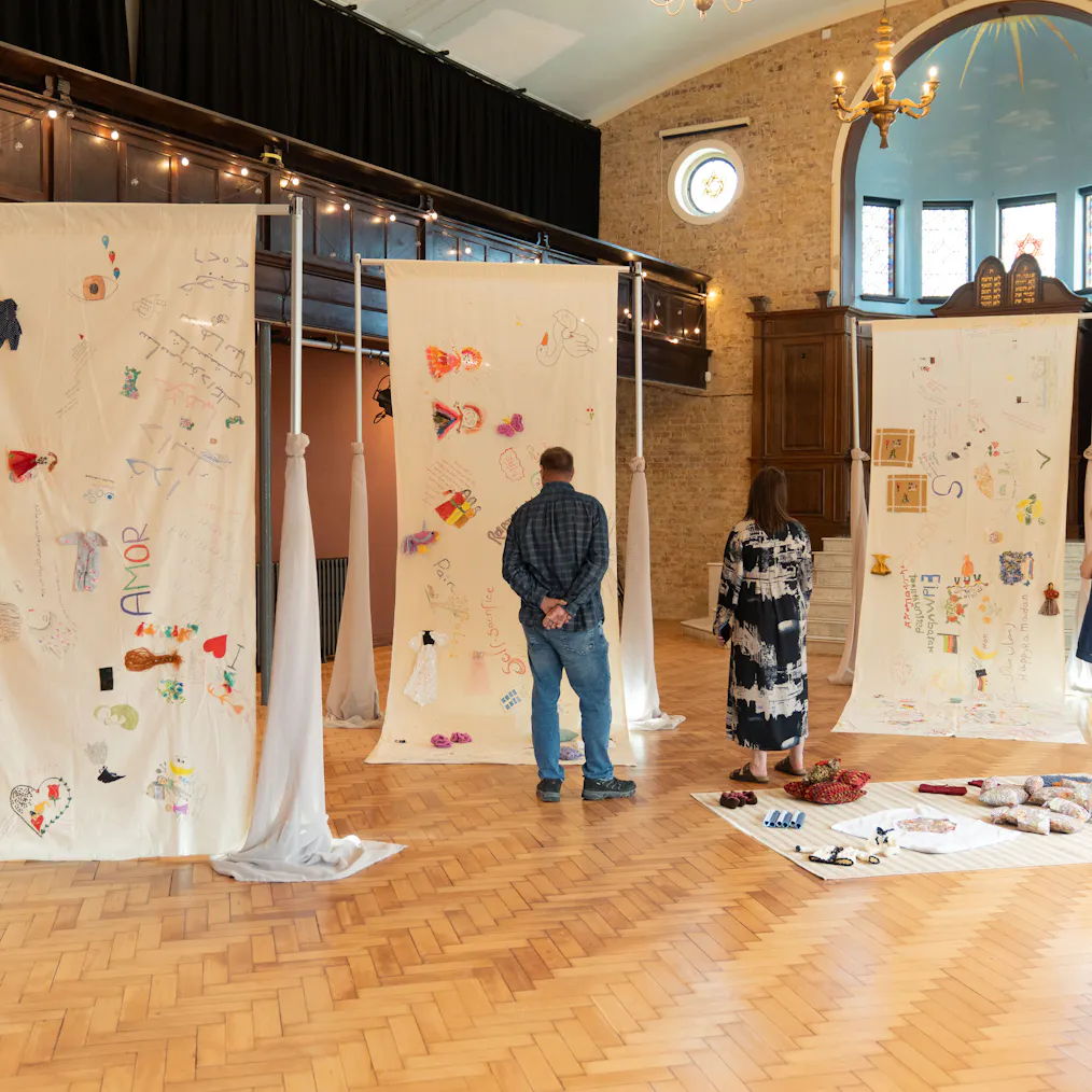 People stranding in an exhibition space. There are tall pieces of clothes hanging with paintings and illustrations