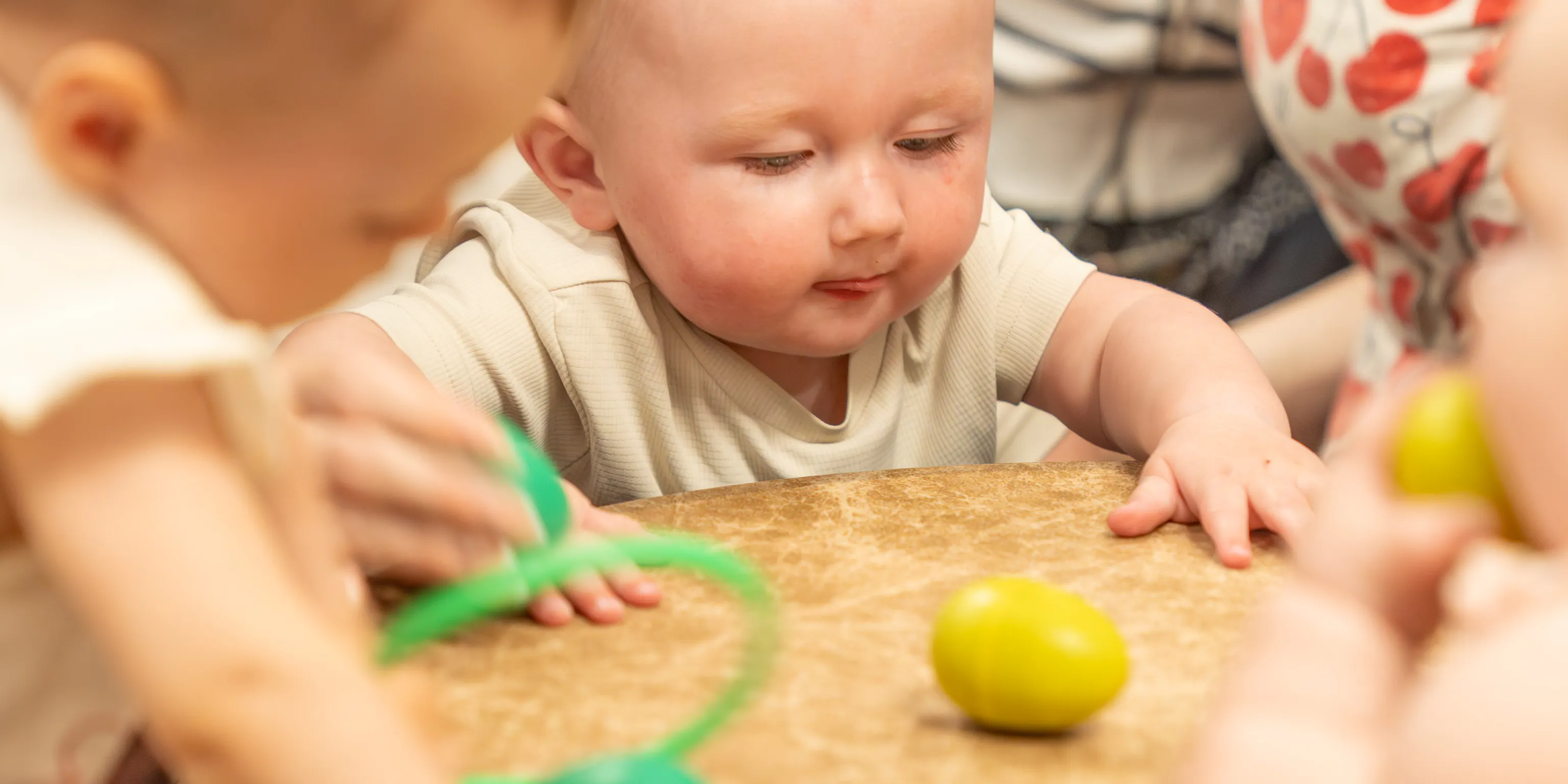 A group of babies and young children gather in front of a colourful drum with egg shaped rattles on it