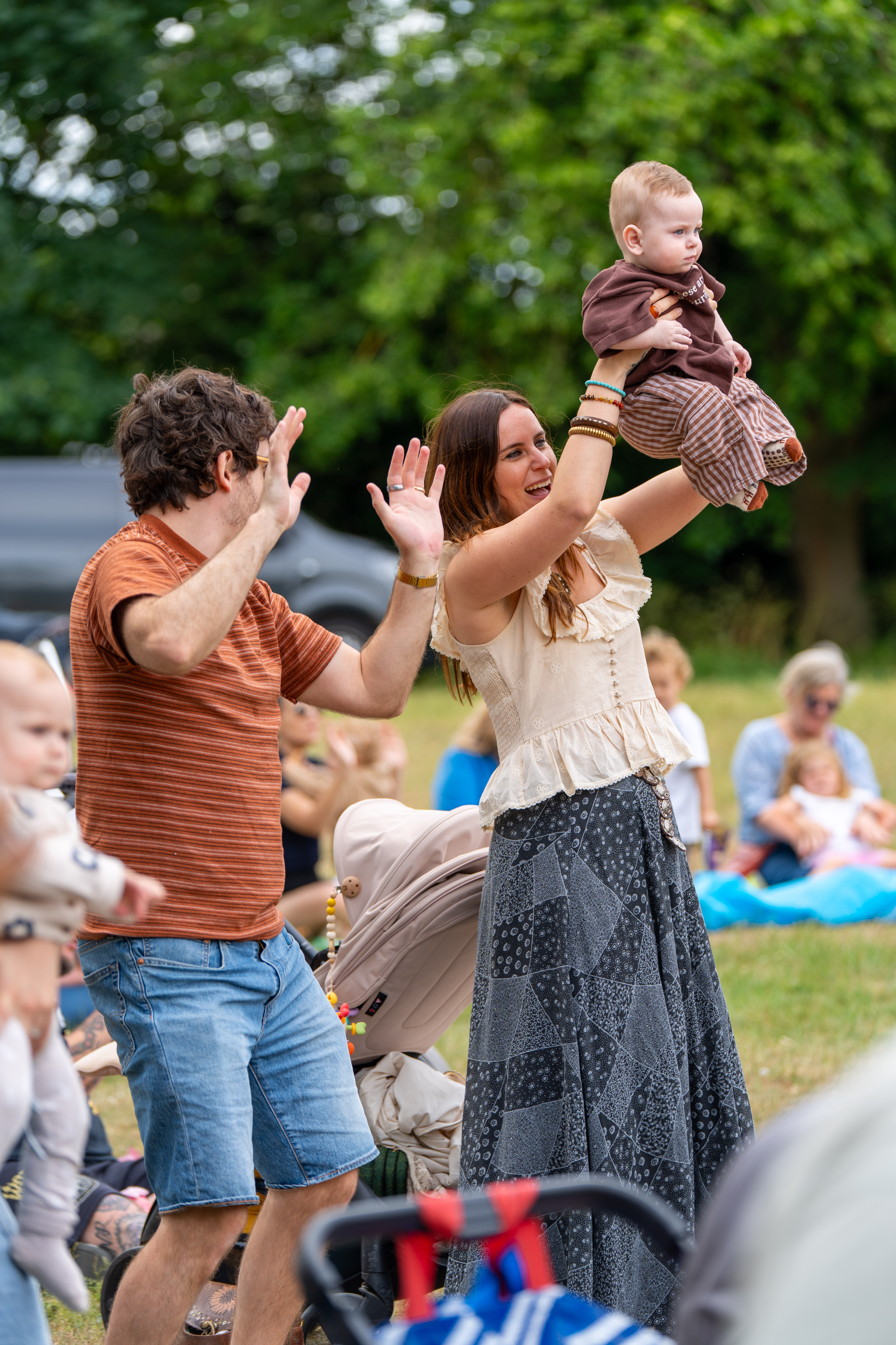 Two parents and a baby dancing to a song. One is holding up their hand and the other holding up the baby 
