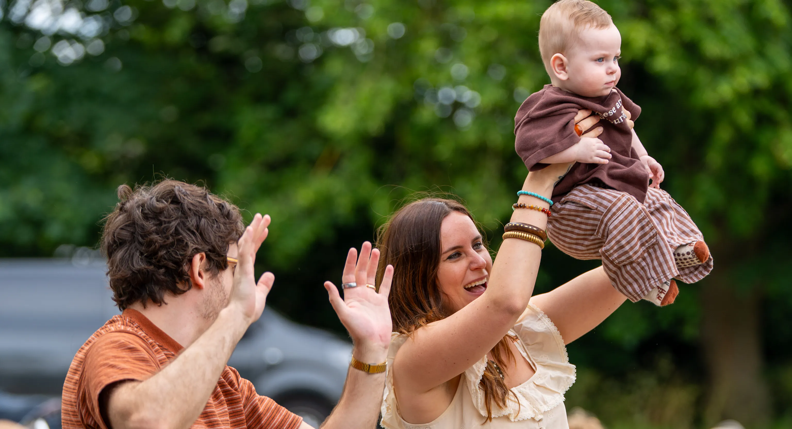 Two parents and a baby dancing to a song. One is holding up their hand and the other holding up the baby