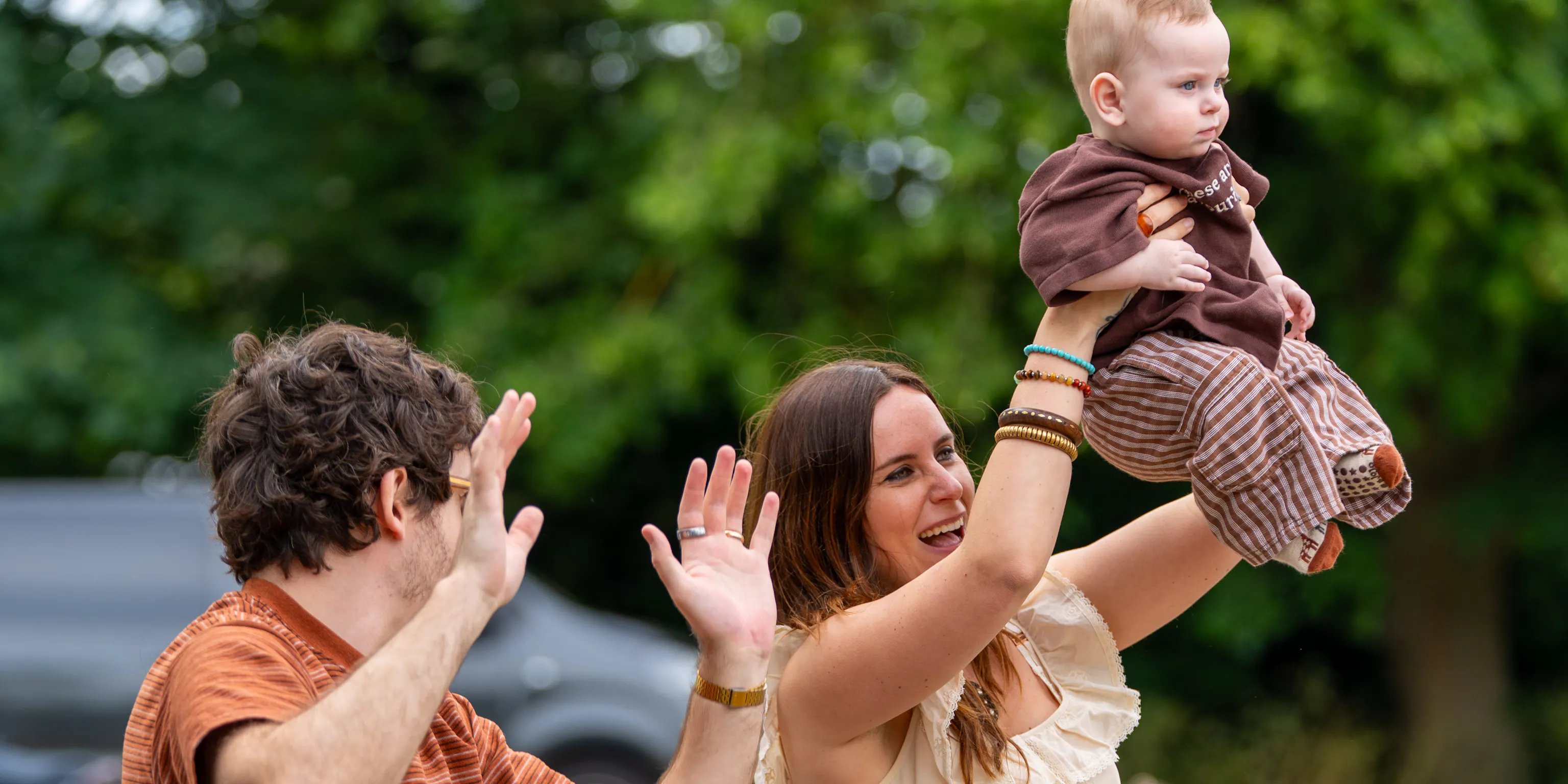 Two parents and a baby dancing to a song. One is holding up their hand and the other holding up the baby
