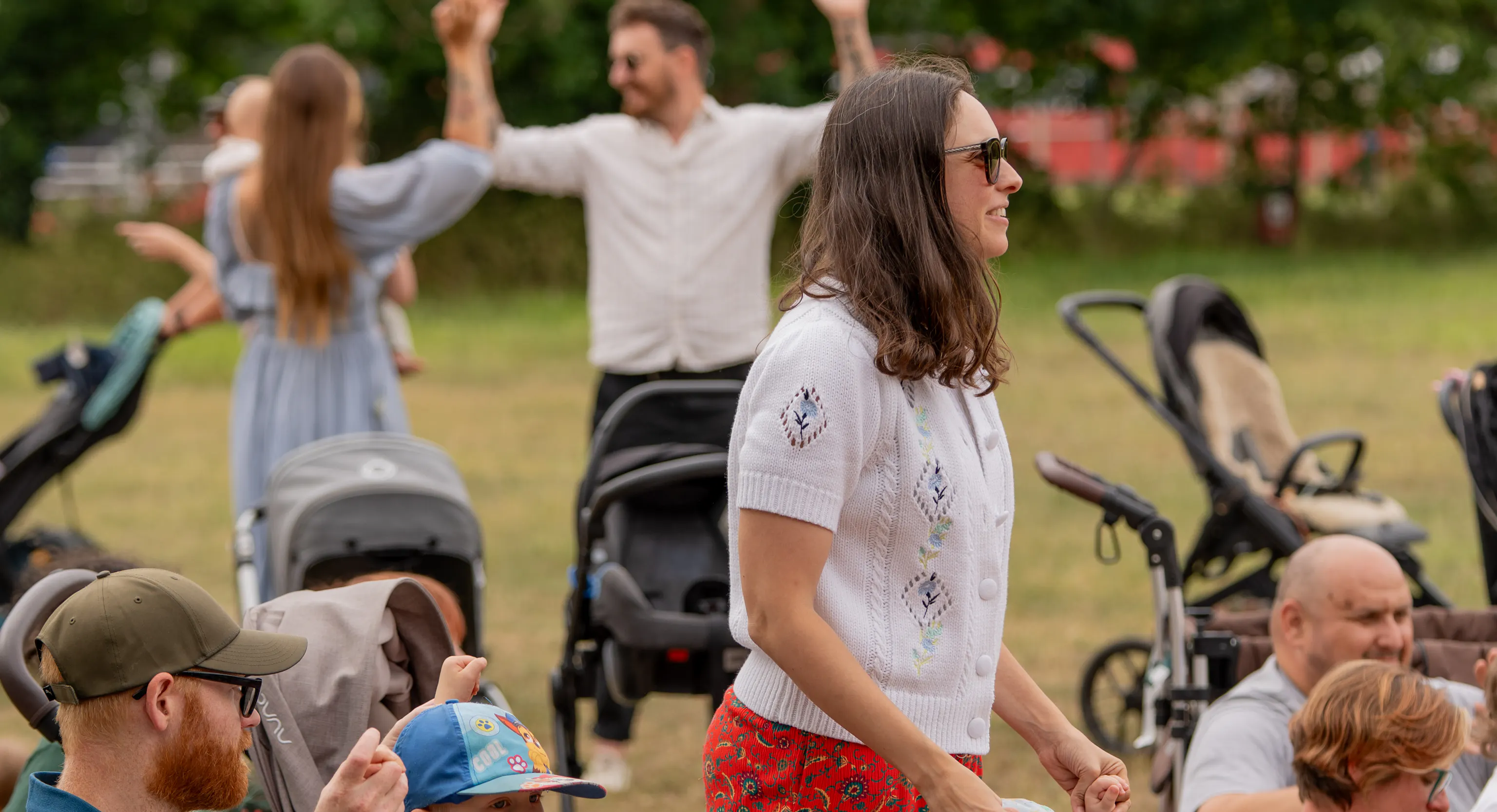 Families in an outdoor park. Some are standing, sitting and others have their hands up