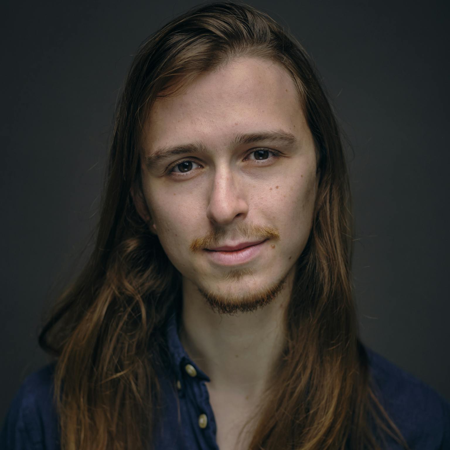 A person looking at the camera in fornt of a dark background