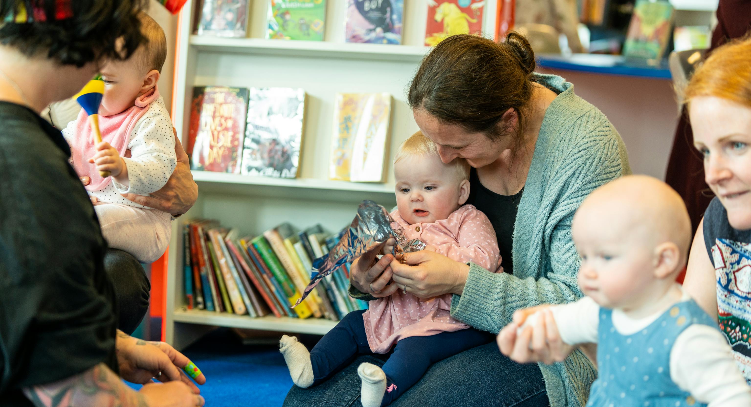 Babies and their parents/carers during a Playground session. There are a mix of babies sat or standing next their their parents/carers in a library
