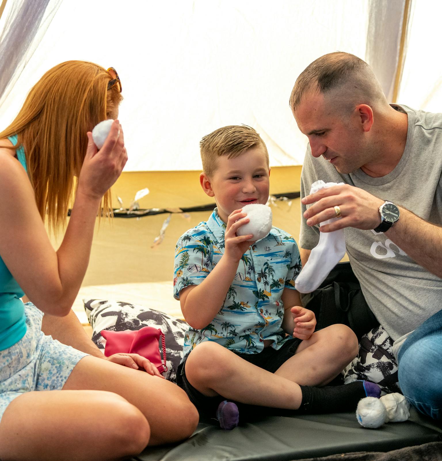 A family sat together on the floor in a tent holding white balls and socks.