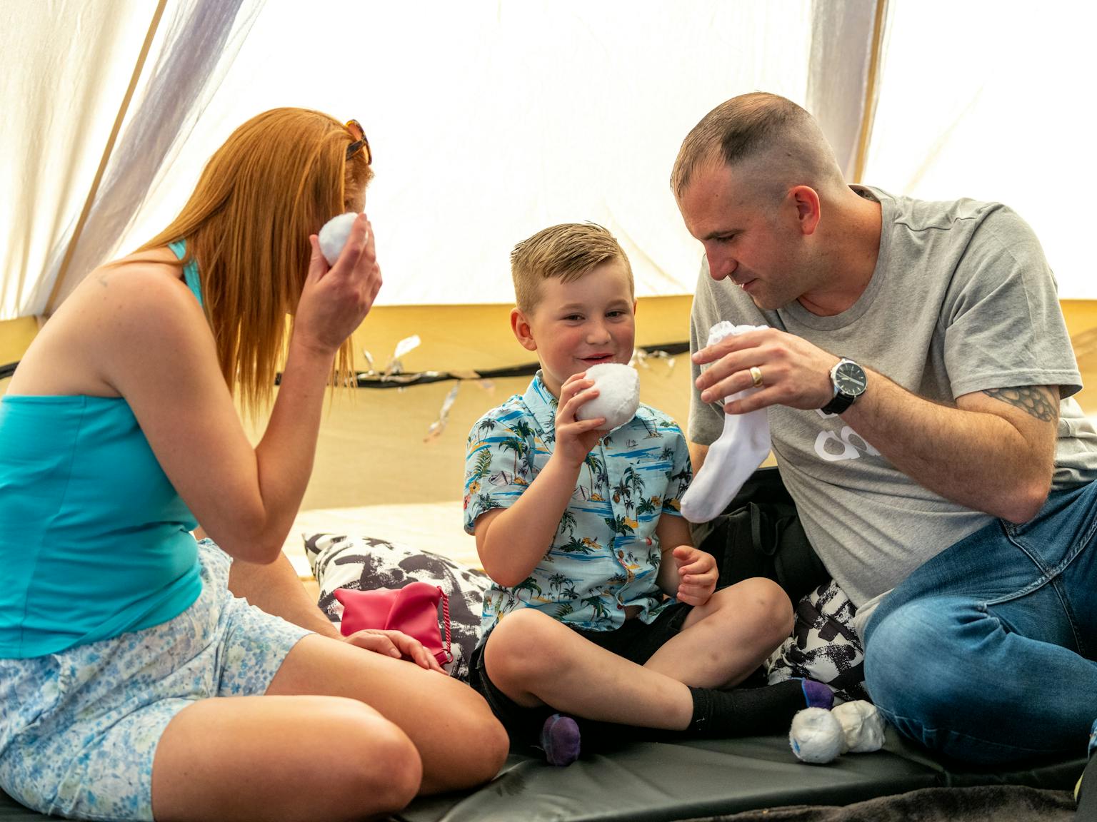 A family sat together on the floor in a tent holding white balls and socks.