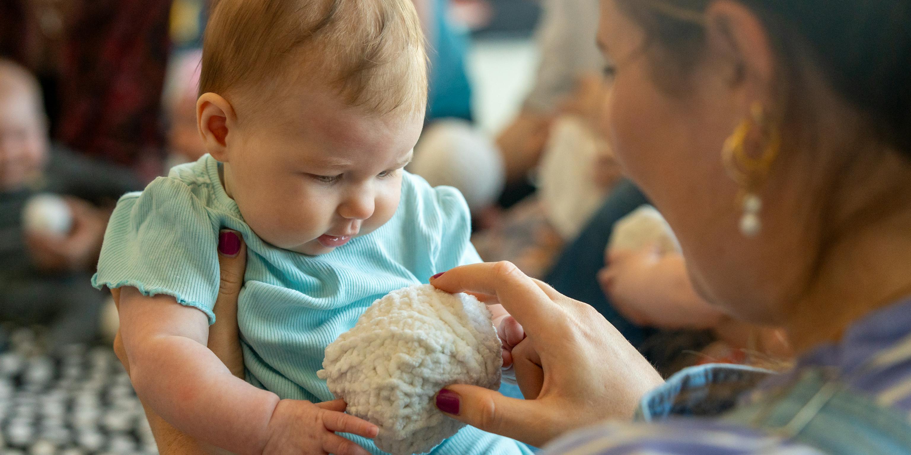 A baby and their parent/carer are holding a textured ball together.
