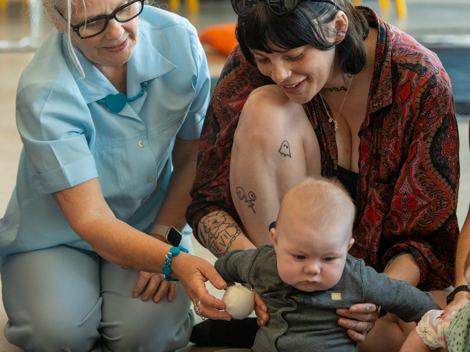 A baby, their parent/carer and Playground artists are sat on a black and white mat during a Baby Playground session
