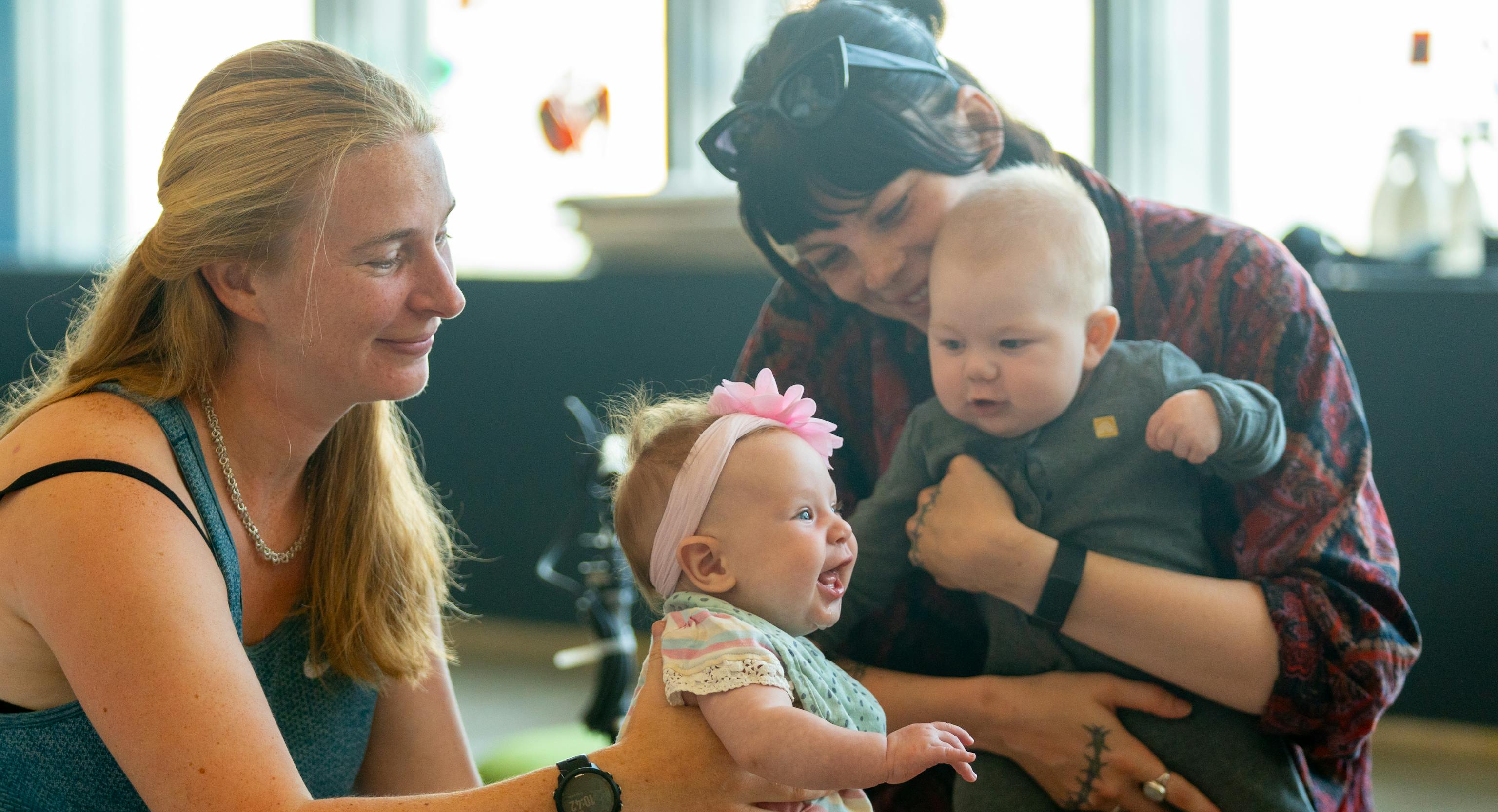 Two babies with their parent/carer during a Playground session. Both parent/carers are holding up the babies.