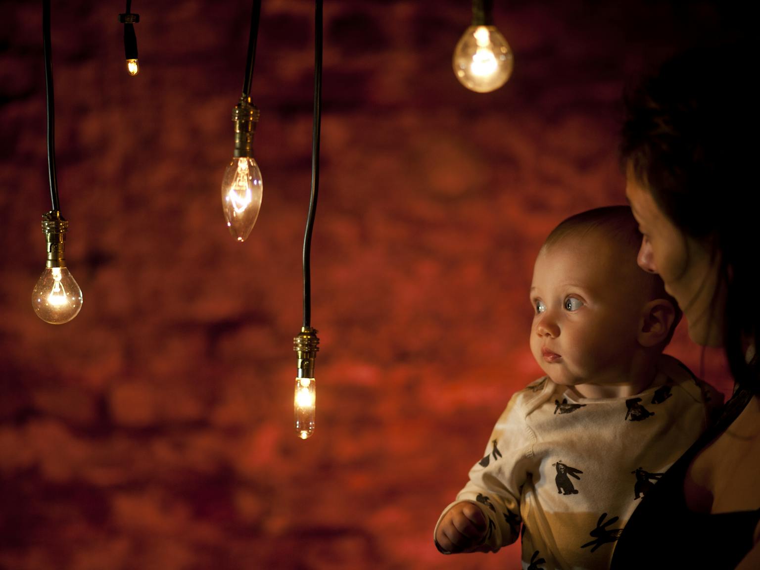 A baby and mother in a darkly lit room surrounded by light