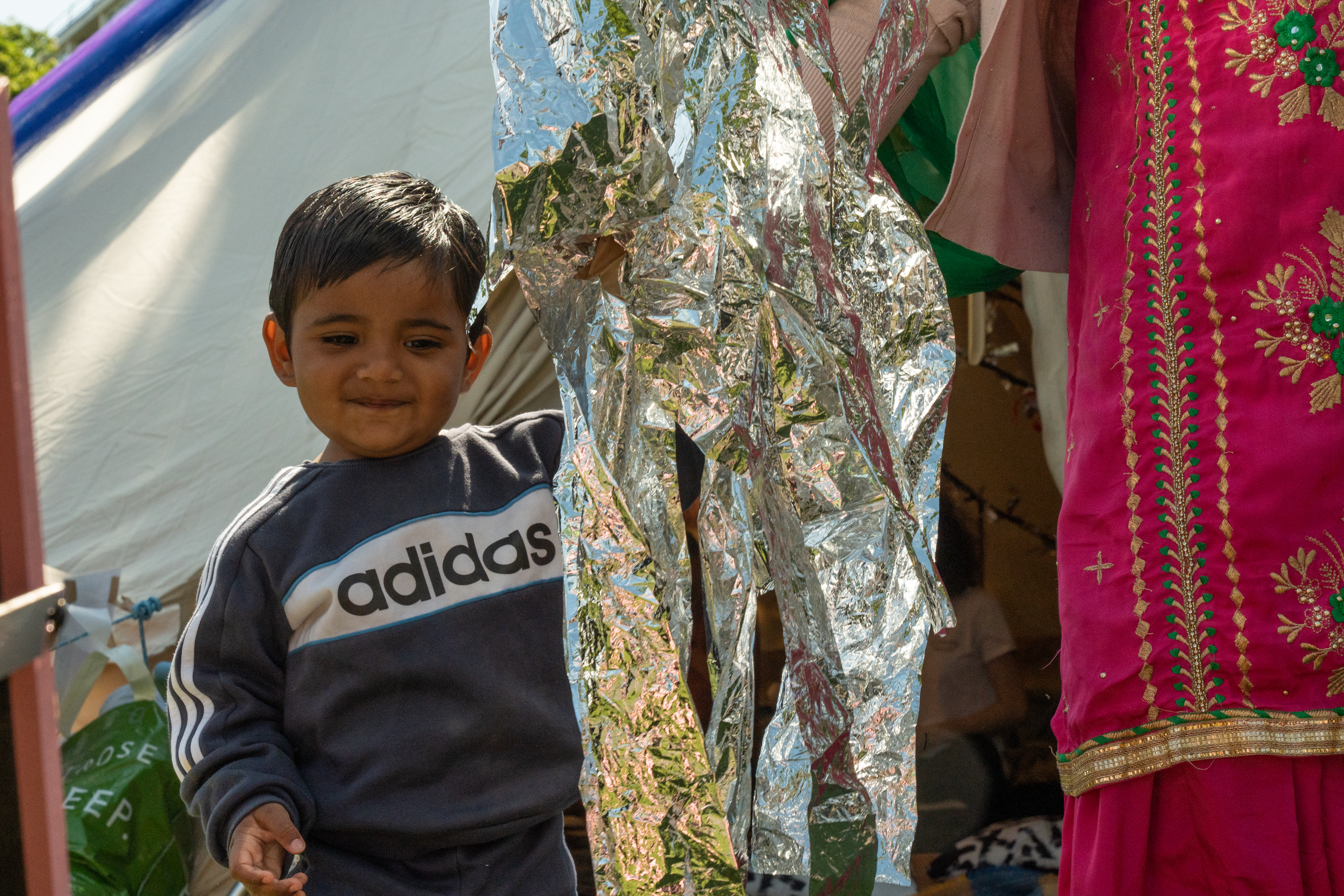 A young child is stood next to their parent/carer and holding hands. Next to them is some reflective foil paper