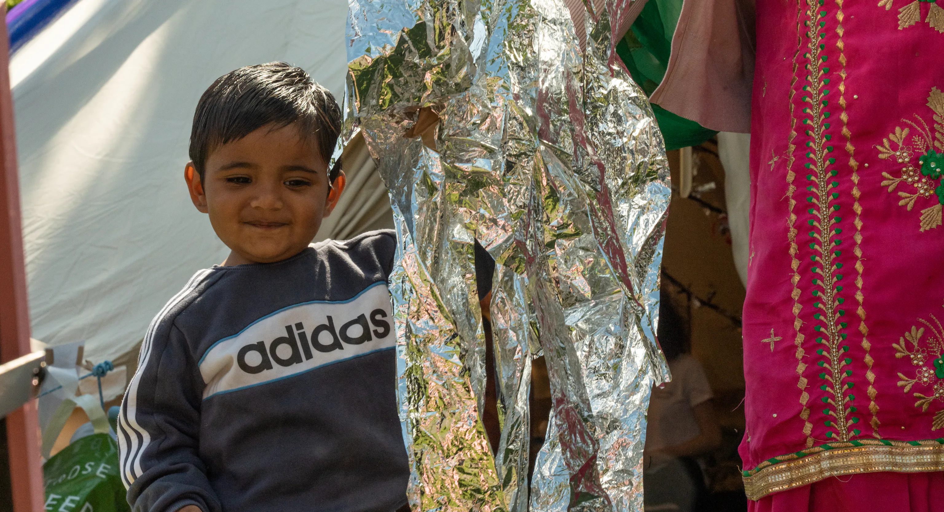 A young child is stood next to their parent/carer and holding hands. Next to them is some reflective foil paper