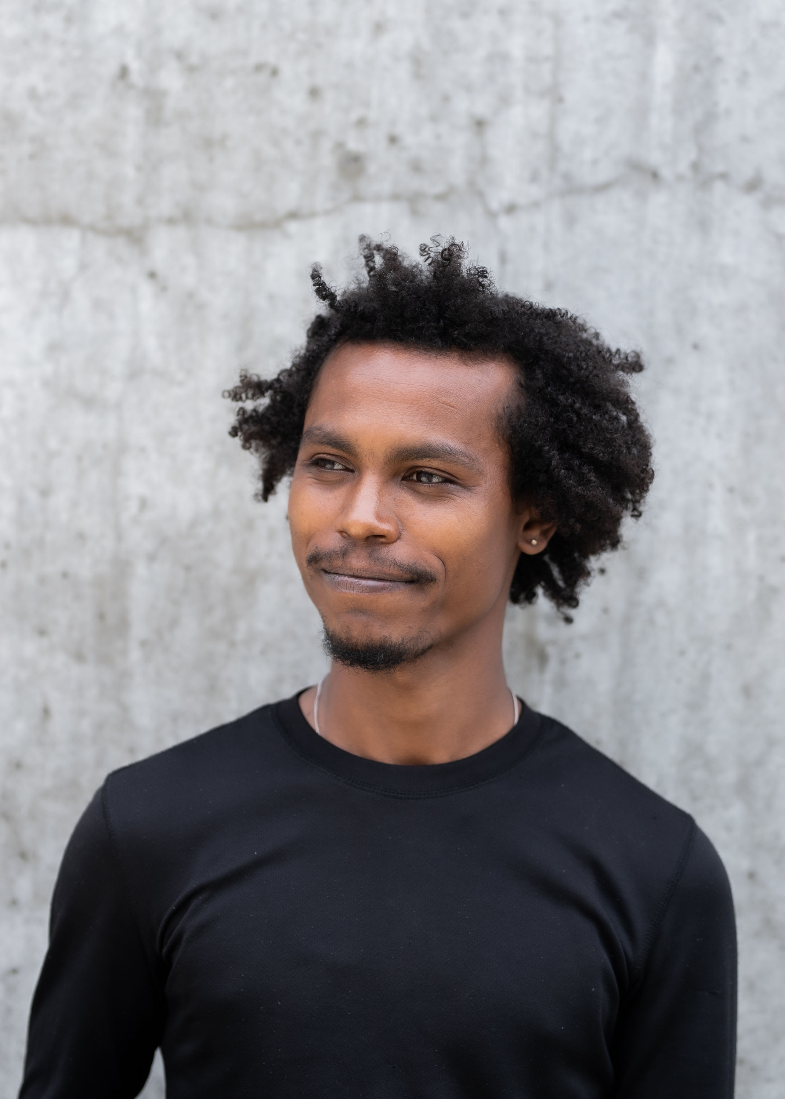 A person looking to the side and smiling. They are stood behind a light grey background.