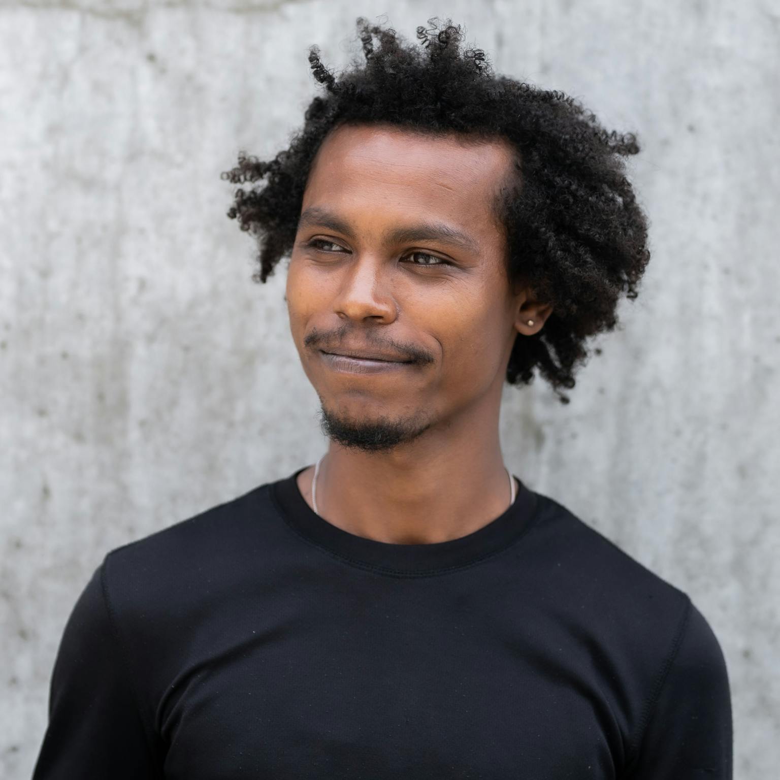 A person looking to the side and smiling. They are stood behind a light grey background.