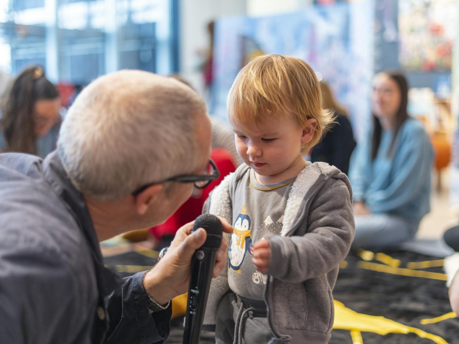 An artist is holding up a microphone to a baby who is reaching over for it