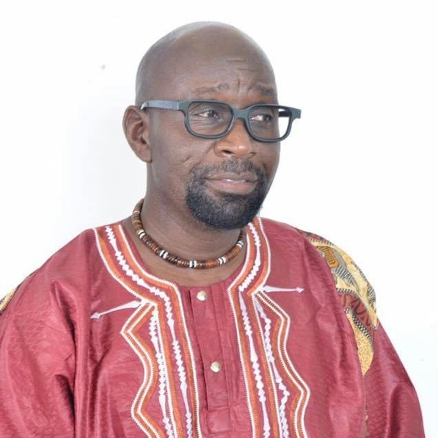 Lucky is stood in fornt of a white background and looking away from the camera. He is wearing a colourful print shirt.