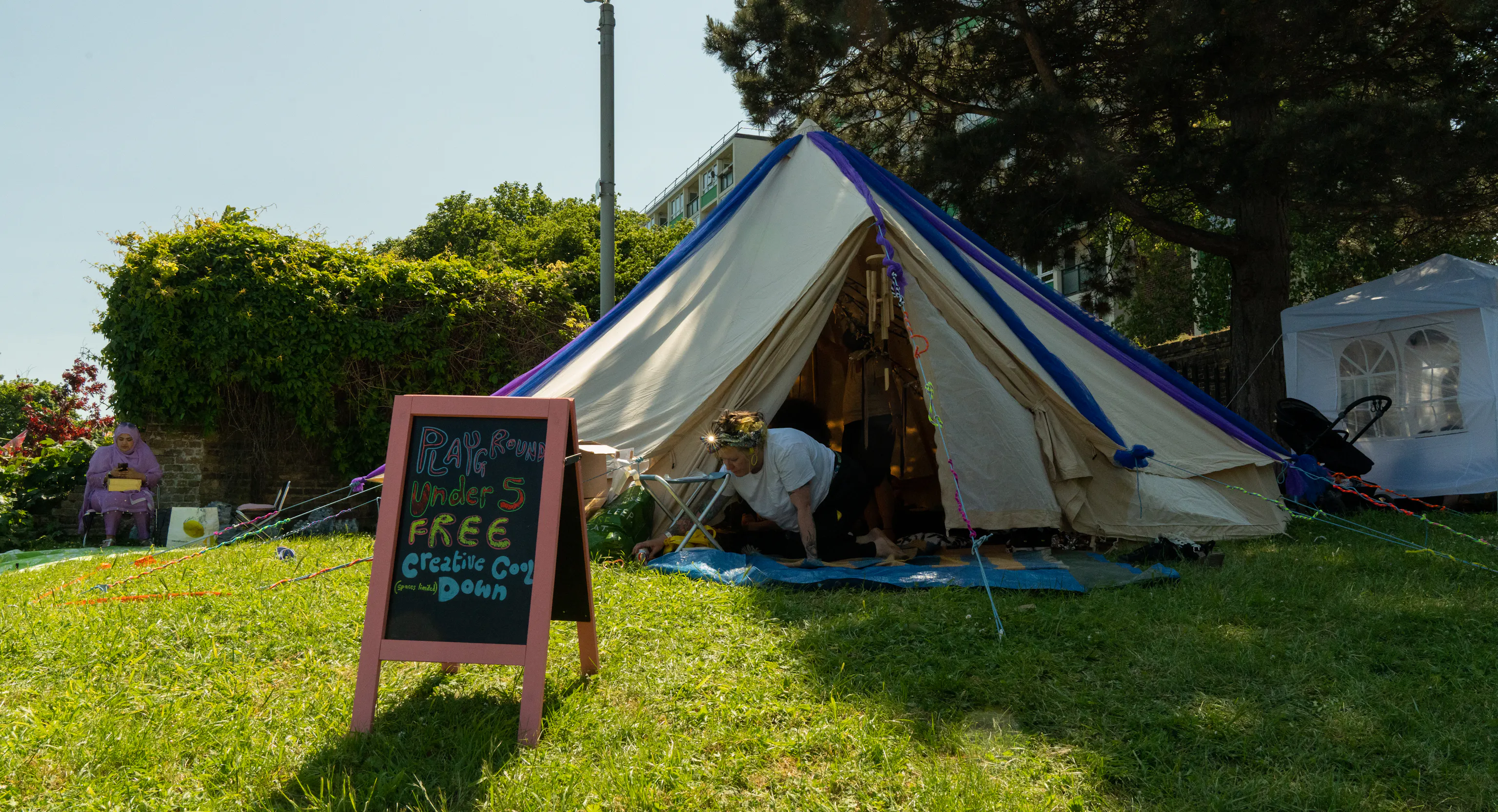 A tipi tent set up outdoors on grass. In fornt of it is a board that says Playground, Free Cool Down