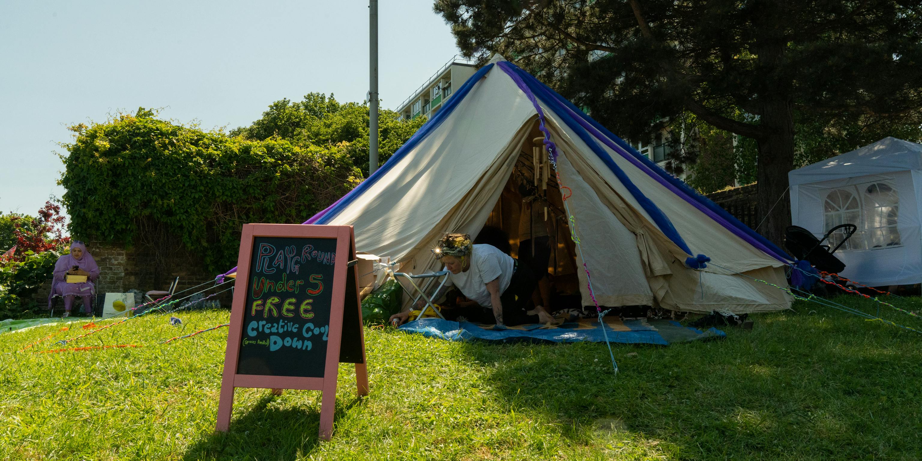 A tipi tent set up outdoors on grass. In fornt of it is a board that says Playground, Free Cool Down
