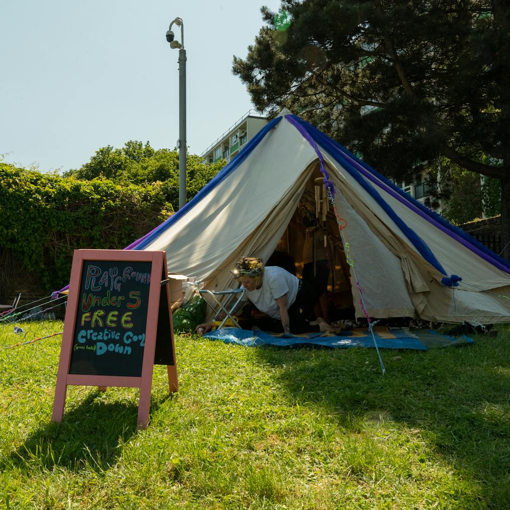 A tipi tent set up outdoors on grass. In fornt of it is a board that says Playground, Free Cool Down