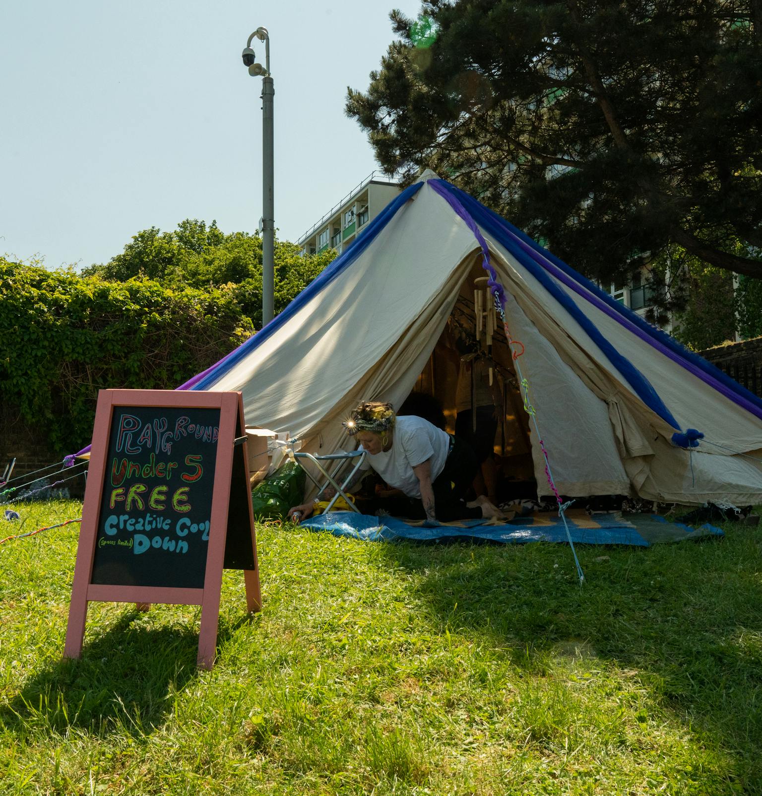 A tipi tent set up outdoors on grass. In fornt of it is a board that says Playground, Free Cool Down