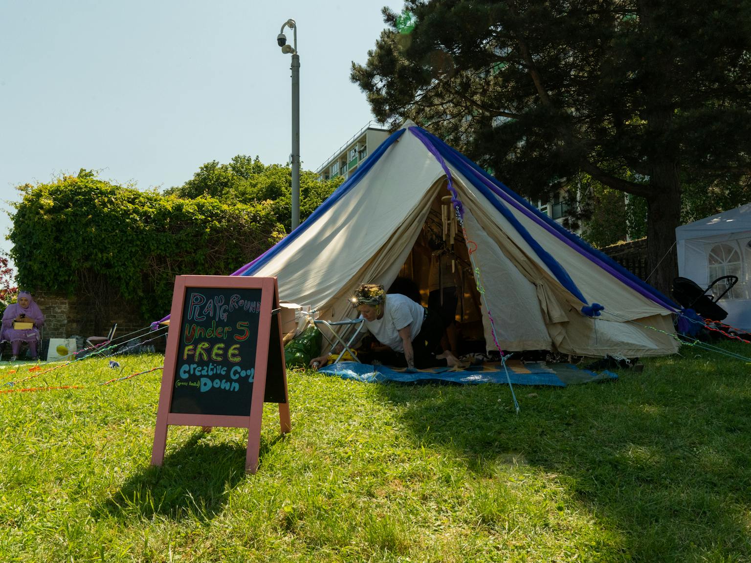 A tipi tent set up outdoors on grass. In fornt of it is a board that says Playground, Free Cool Down