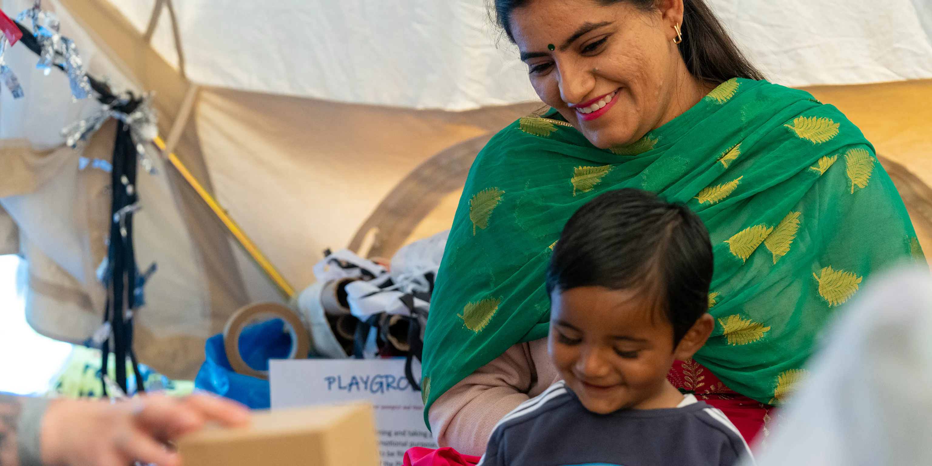 A parent/carer sits behind a young child.